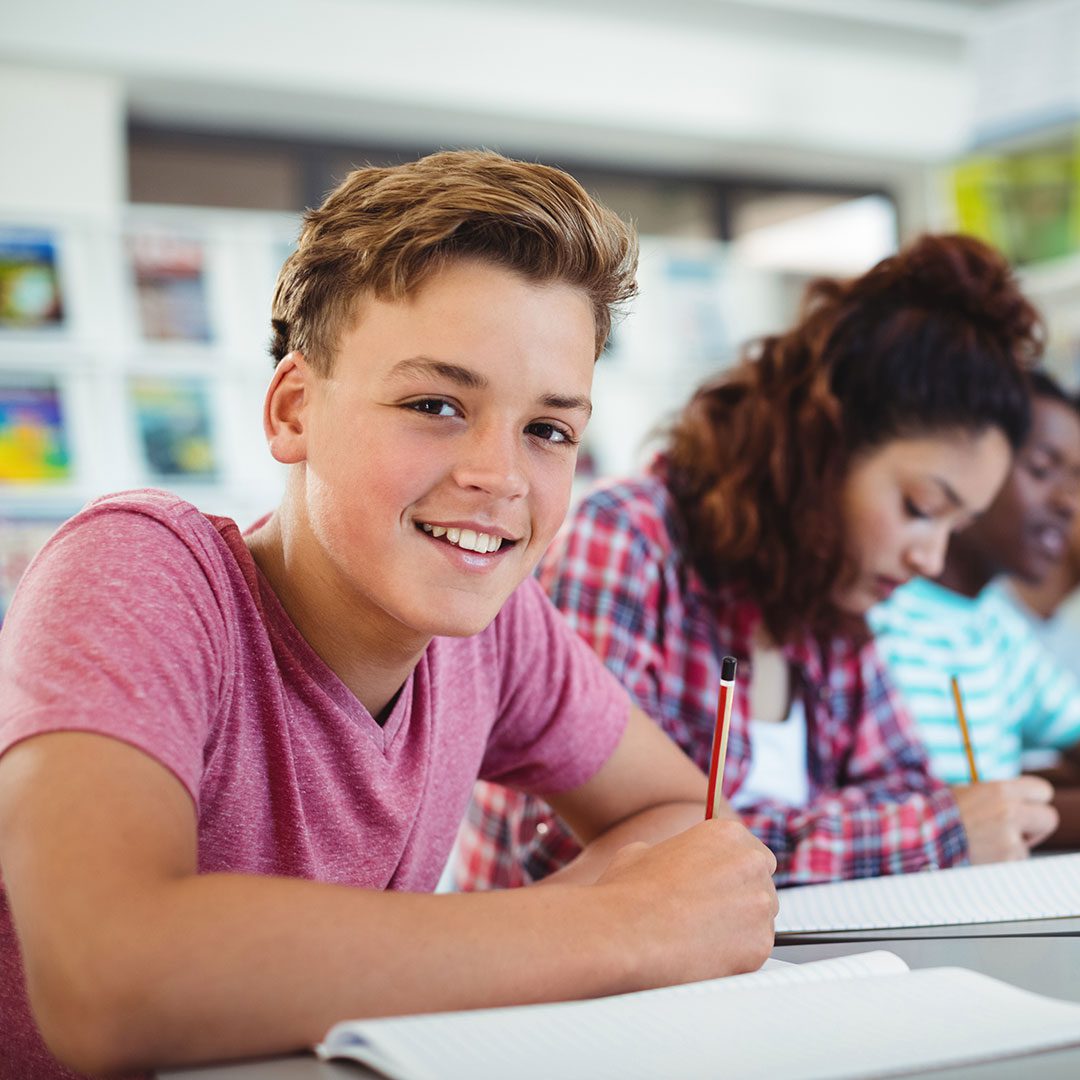 closeup of a high school student smiling while peers work on homework